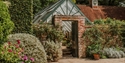 Glasshouse and walled garden at Pashley Manor Gardens with flowering borders and paved pathways.