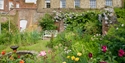 Lamb House garden with circular fountain surrounded by colourful flowers and historic Rye rooftops.