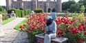 Herstmonceux Castle with vibrant rose gardens and sculpture in the historic estate grounds.