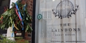 Exterior sign for The Laindons Guest House with shell logo and decorative greenery on brick frontage.