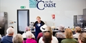 a photograph of a cookery classroom with a teacher, CJ Jackson, in the front, rows of backs of heads.