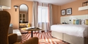 Interior view of The Relais Cooden Beach. Shows large double bedroom with red and white chevron carpet and armchair in foreground.