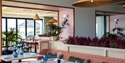 Interior view of The Relais Cooden Beach. Shows restaurant area with blue glasses on table and large windows to outside view.