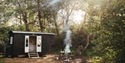 Shepherd’s hut by The Original Hut Company near Bodiam, with a smoking fire pit and wooden seating in a woodland clearing.