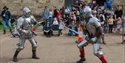 Two knights in full armour sword-fight before a crowd at an outdoor medieval re-enactment.