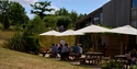 Outdoor seating area at The Hub near Bodiam, with people dining under large parasols beside the wooden building.