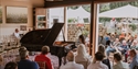 Audience watching a pianist perform on a grand piano in an open pavilion at the Hastings International Piano concert.