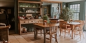 Cosy café interior at King John’s Nursery with wooden tables, chairs, plants, and rustic shelving display.