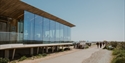 Modern glass-fronted Rye Harbour Discovery Centre beside coastal path, with visitors, seating area and sea views.