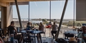 View from inside Rye Harbour Discovery Centre café with visitors seated, overlooking coastal path and nature reserve.
