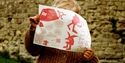 Child holding a red illustrated “Castle Explores” leaflet in front of a stone wall at Hastings Castle.