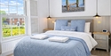 Bright bedroom at Beside The Sea Holidays with a blue bedspread, coastal artwork, and large window overlooking houses