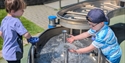 Children explore a water exhibit at The Observatory Science Centre, interacting with bubbling water and valves.