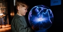 Child explores a plasma globe exhibit at The Observatory Science Centre, watching electric arcs respond to touch.