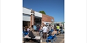 People socialising outside Flatland Projects in Bexhill, with seating and an ice cream van on a sunny day