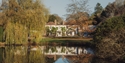 Crafted at Powdermills Hotel reflected in a lake, surrounded by autumn trees, showcasing serene countryside setting.