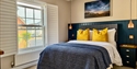 Cosy bedroom at Beside The Sea Holidays with navy panelling, yellow cushions, and a large window overlooking the street.