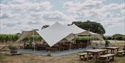Covered outdoor seating area at Gusbourne Estate with long tables set among vineyard rows.