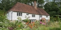 Traditional white weatherboard cottage with red tiled roof, surrounded by colourful wildflower garden and greenery.
