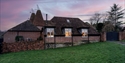 Brick cottage at dusk with lit windows, traditional tiled roof, oast-style chimneys and enclosed garden.
