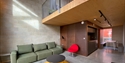 Modern Barnscape Farm interior with green sofa, red chair, mezzanine level, and compact kitchen in a minimalist design.