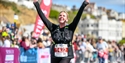 picture shows a person who has just finished a running event. They are smiling and throwing their hands up.