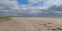Wide sandy stretch of Camber Beach with dune grasses on the left under a cloudy sky.