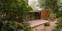 A suspended rectangular wooden lodge with large glass facade in a wooded landscape.