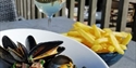 Close up of a table outside at bexhill restaurant pebbles showing a bowl of mussels, bowl of chips and glass of wine.