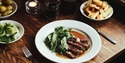 view of gastropub dining with plate of beef and spinach with side plates of vegetables and chips