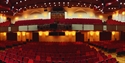 wide angle view of an auditorium, taken from the stage. Shows circle and stalls seating, all red chairs.
