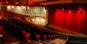 Auditorium view taking from stairs in the circle area. Shows red seats in curved formation looking down towards red curtain stage.