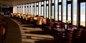 view of the cafe with a stretch of tables and chairs against a window facade with views of the beach and sea.