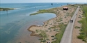 aerial view of a harbour, with grass and vegetation, single shore and a long tarmac path leading along the shoreline.