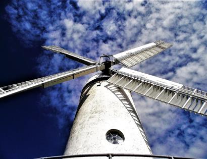 a photograph of a white windmill against a blue sky. Taken from below windmill looking upwards.