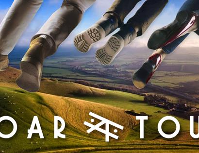 poster for SOAR TOUR shows feet dangling in the sky above rolling green hills