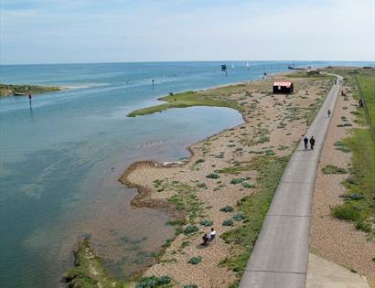 aerial view of a harbour, with grass and vegetation, single shore and a long tarmac path leading along the shoreline.