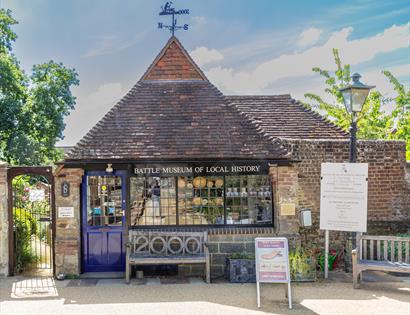 front external view of battle museum. A small brick building with pointed tiled roof with a weathervane on top.