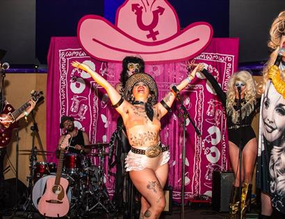 Image shows performers at a Queer cxntry event including a band in the background