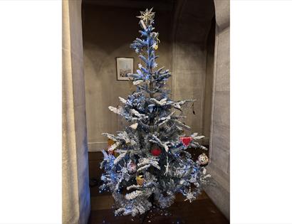 Decorated Christmas tree with silver tinsel, ornaments, and lights in a stone archway.