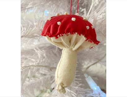 Fabric mushroom ornament with a red cap and white spots hanging on a white Christmas tree.