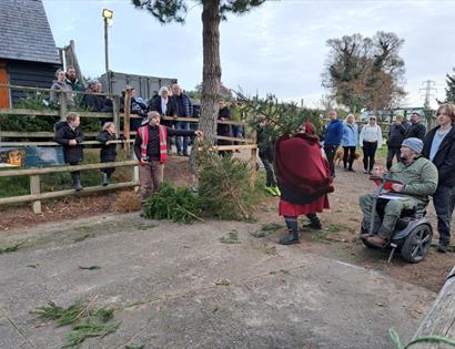 A group gather to watch someone throwing a christmas tree at a previous event.