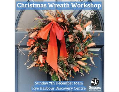 Event image of a seasonal wreath on a navy door. The wreath is textured and wild with fresh greenery, dried foliage, berries, and long ribbon tails in