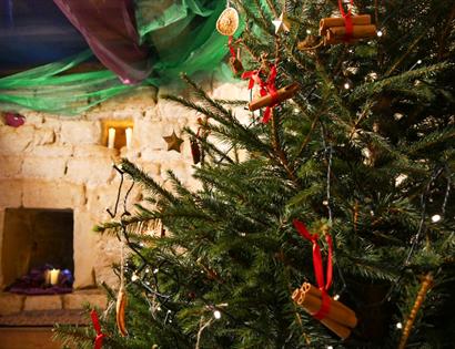 Christmas tree with rustic decorations inside Bodiam Castle, with stone wall and candles in background.