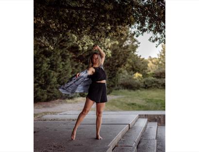 A woman is outdoors on a patio area moving her body. Her clothes flow in the movement.