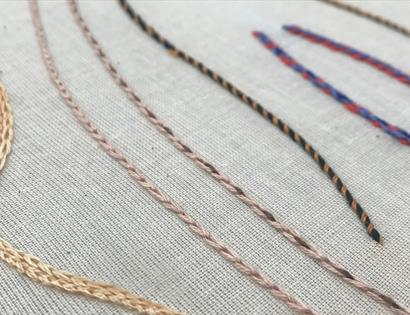 Close-up of braided and twisted threads in various colors laid out on a light fabric background.