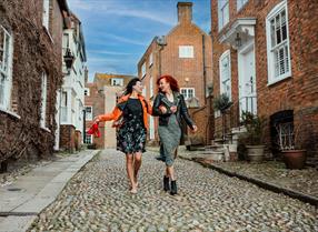 Two young women walk down a cobbled street in Rye.