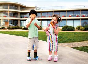 Two children outside the De La Warr Pavilion  building eating ice cream cones. They have ice cream over their faces.