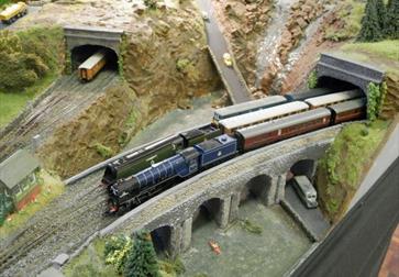 view of a model railway from above. Two trains are crossing a bridge, coming out of a tunnel.
