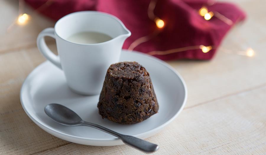 Christmas pudding on a white plate next to a jug of cream.